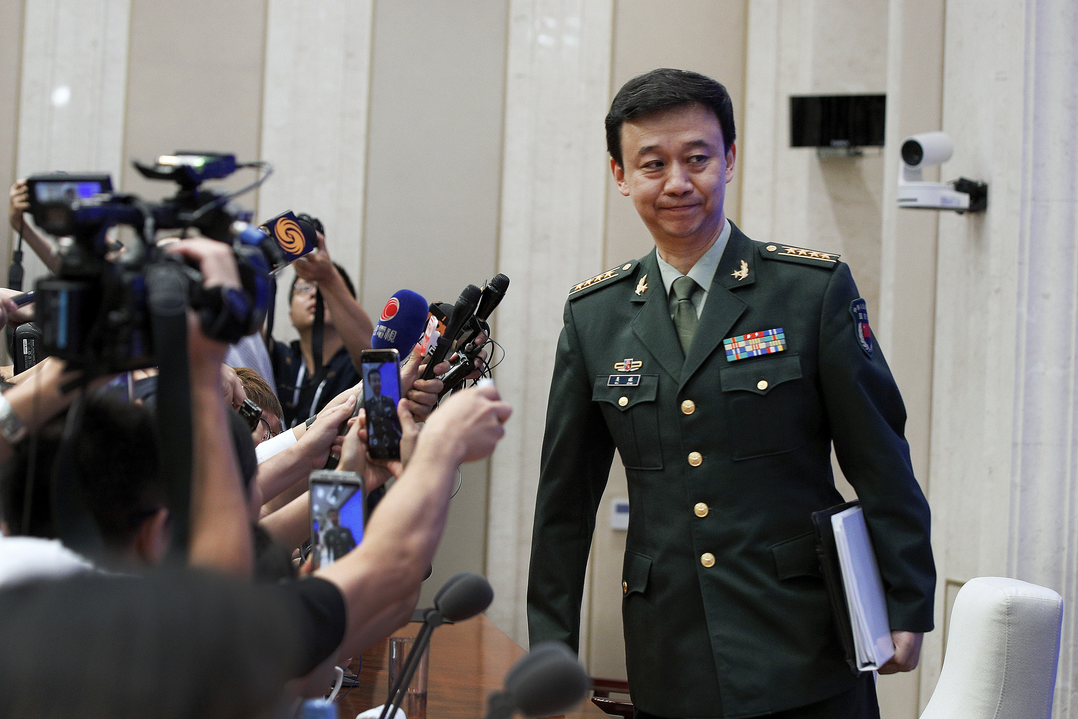 A man wearing military attire standing in front of journalists.