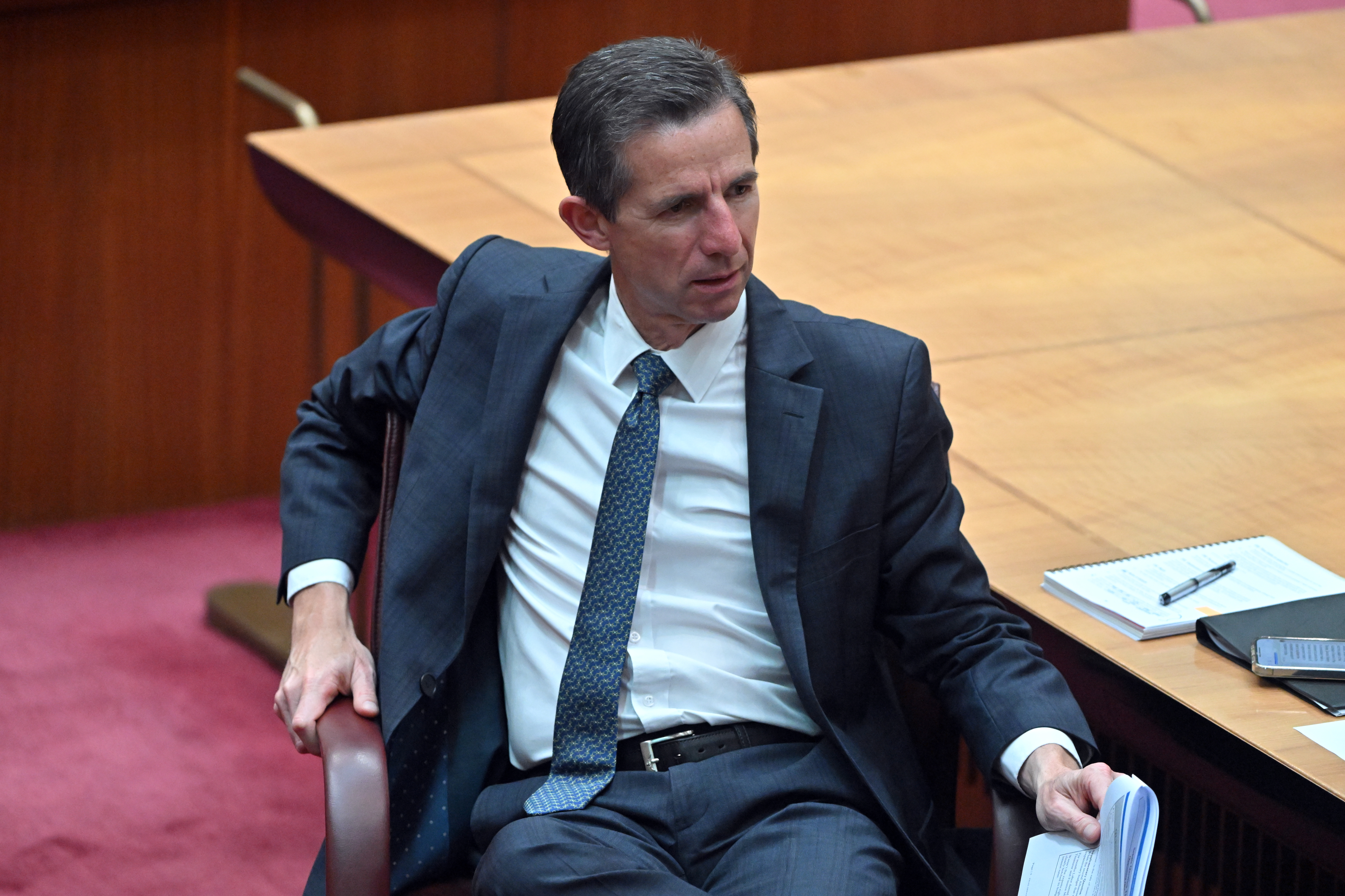 A man wearing a suit and tie seated in a chair.