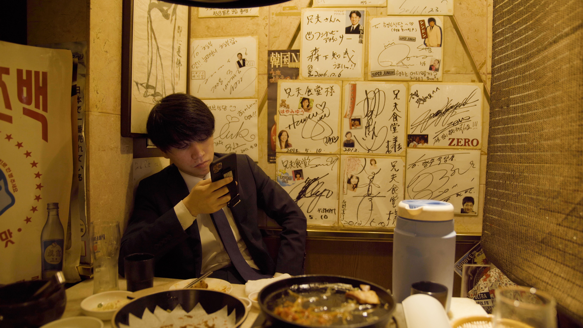 A young man sits in a restaurant while looking at his mobile phone.