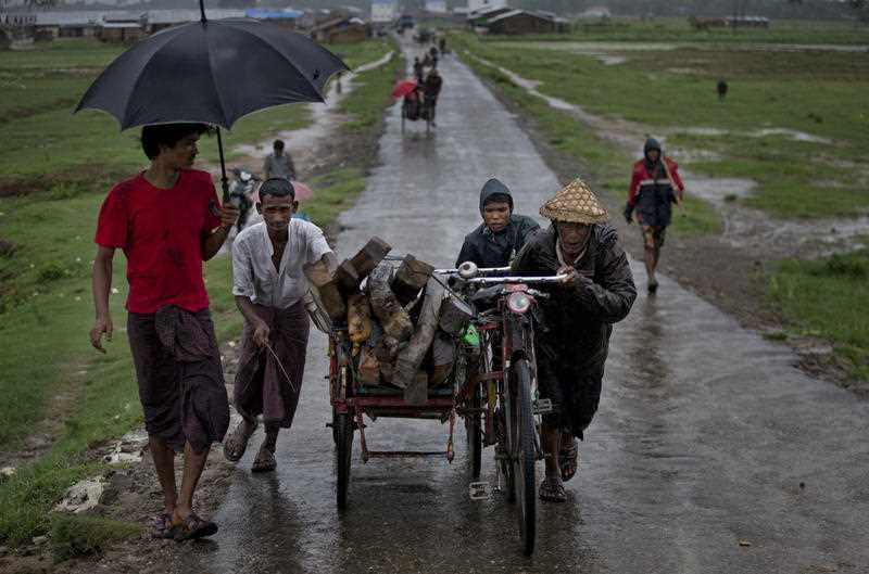 In this June 26, 2014 file photo, Rohingya people push a cart loaded with fire-wood during rain in Thet Kabyin village, close to Sittwe, Rakhine state, Myanmar.