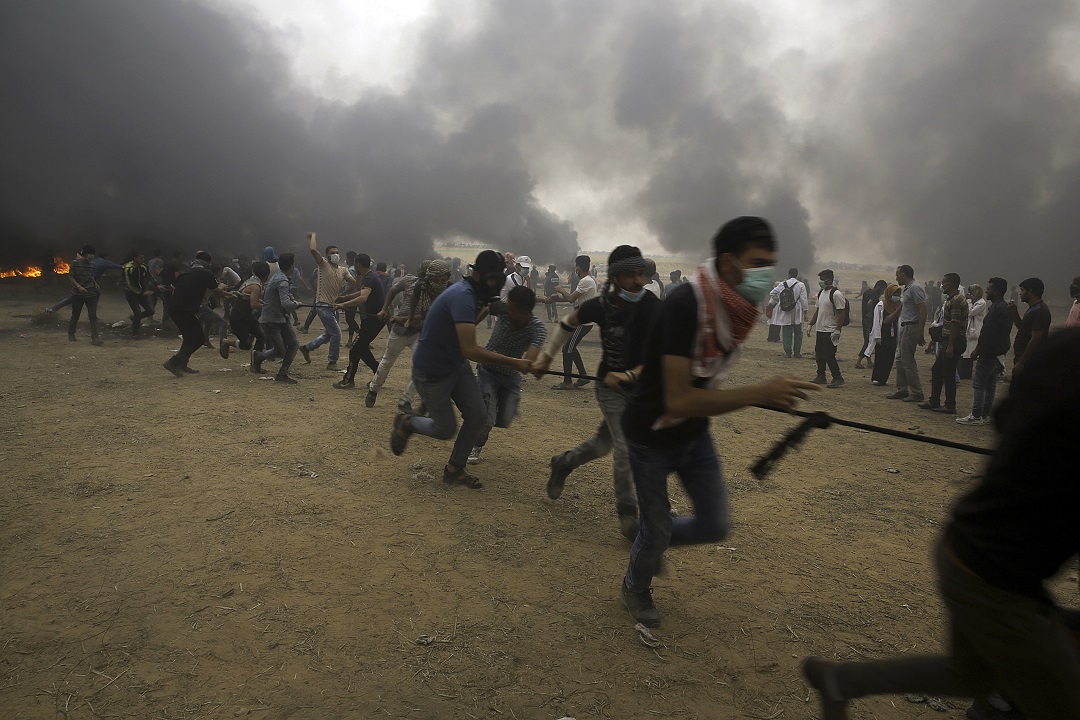 Palestinian protesters try to pull down the fence of the border after they burn tires during a protest at Gaza's border with Israel.