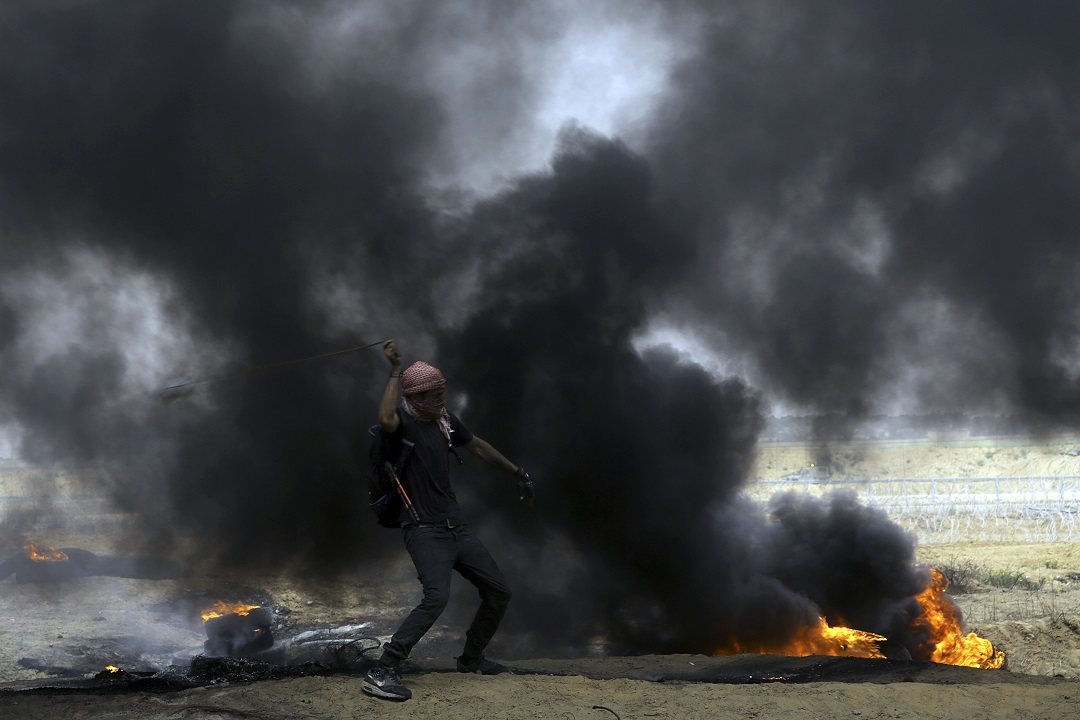 A Palestinian protester hurls stones at Israeli solders near the fence after they burn tires during a protest at Gaza's border with Israel.