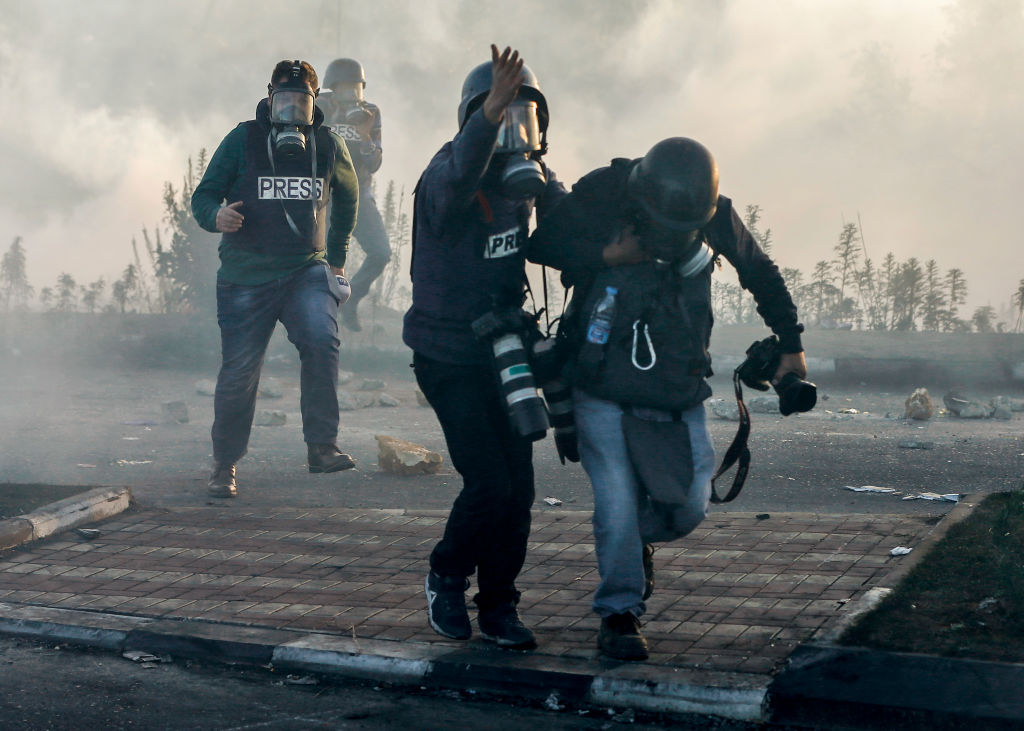Photojournalists and video journalists wearing gas masks flee from teargas fired by Israeli forces on the West Bank.