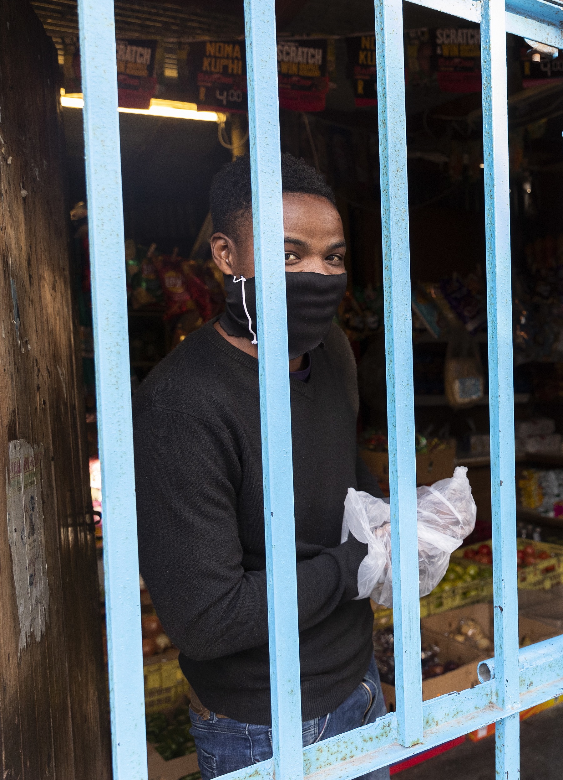 A Spaza shop owner looks out from his shop, which is locked behind bars during the national lockdown.