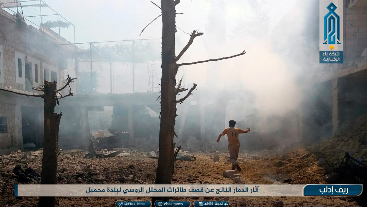 A man is seen running as smoke rises over buildings that were hit by airstrikes, in Mahambal village in Idlib.