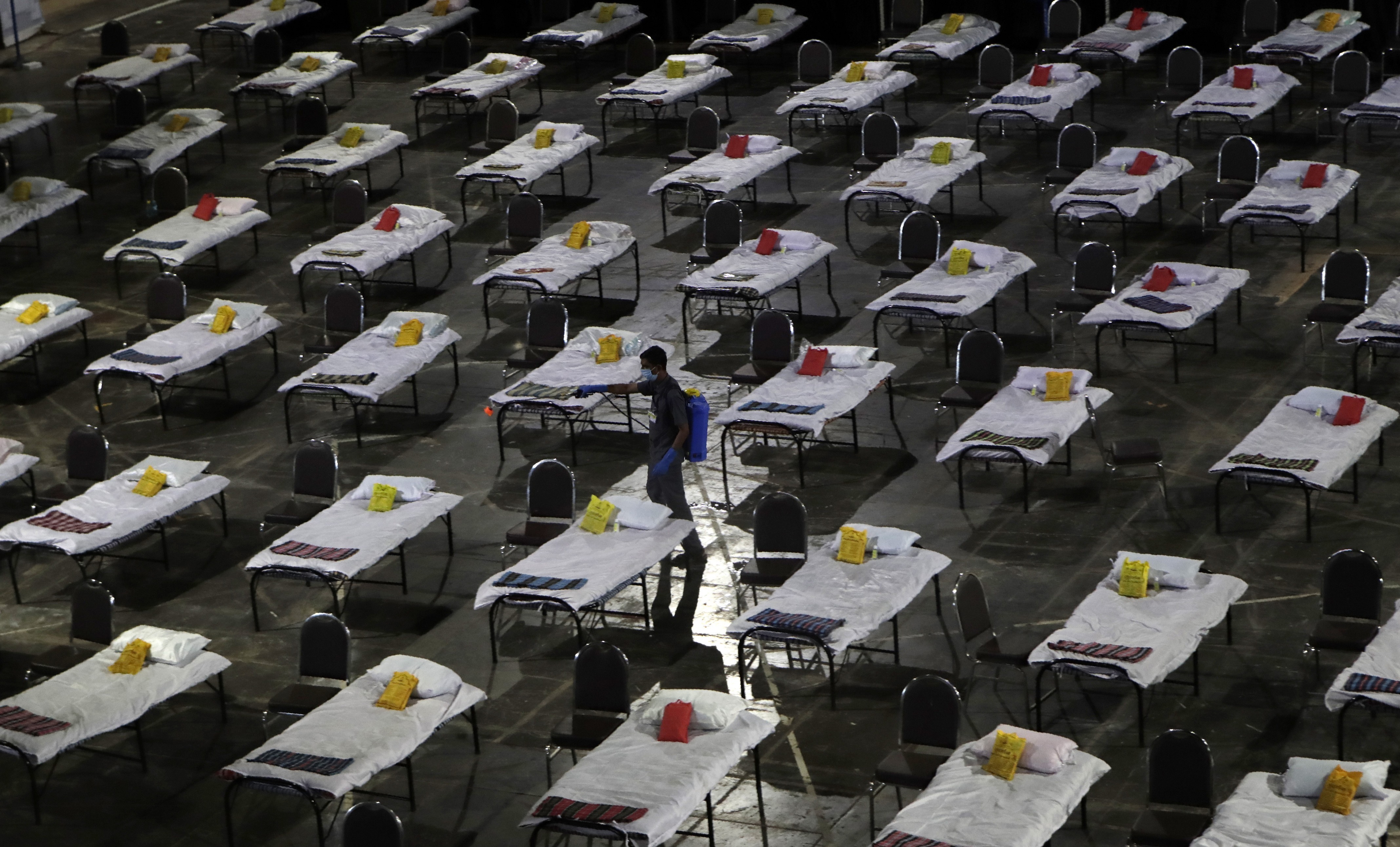 A civic worker sprays disinfectant on beds at a special temporary hospital facility for COVID-19 patients in Mumbai, India, Friday, April 10, 2020.