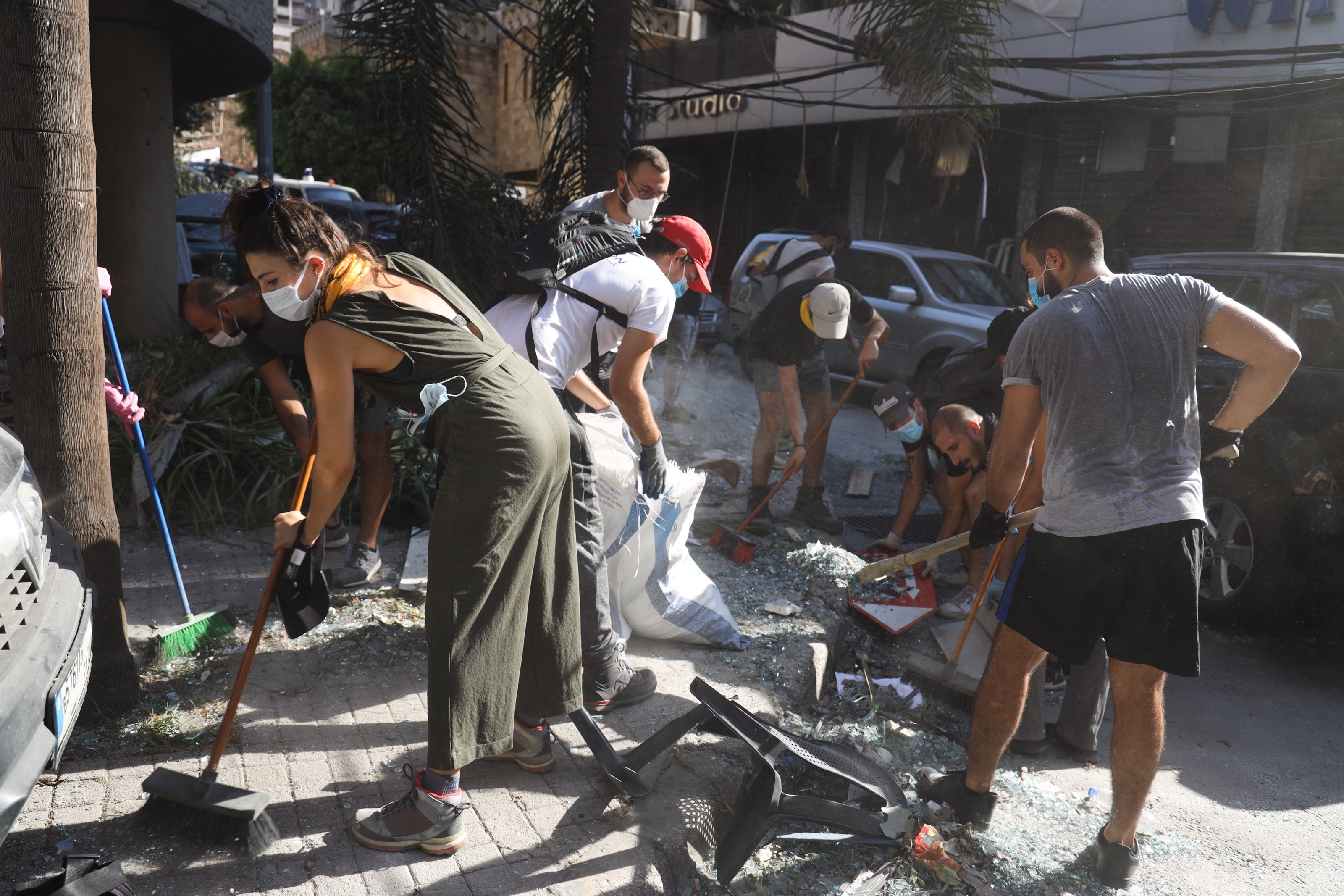 Lebanese youth clear glass debris in a street, one day after an explosion at the Beirut Port.