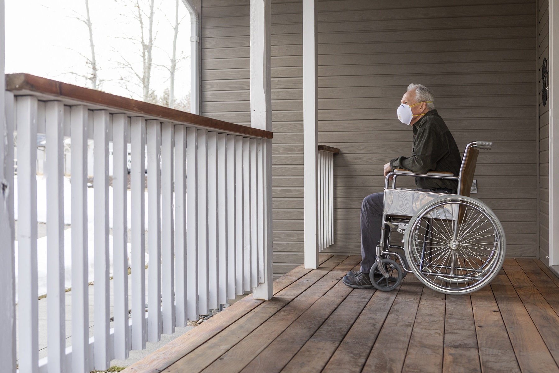 Senior man in wheelchair wearing protective mask to prevent coronavirus transmission on porch