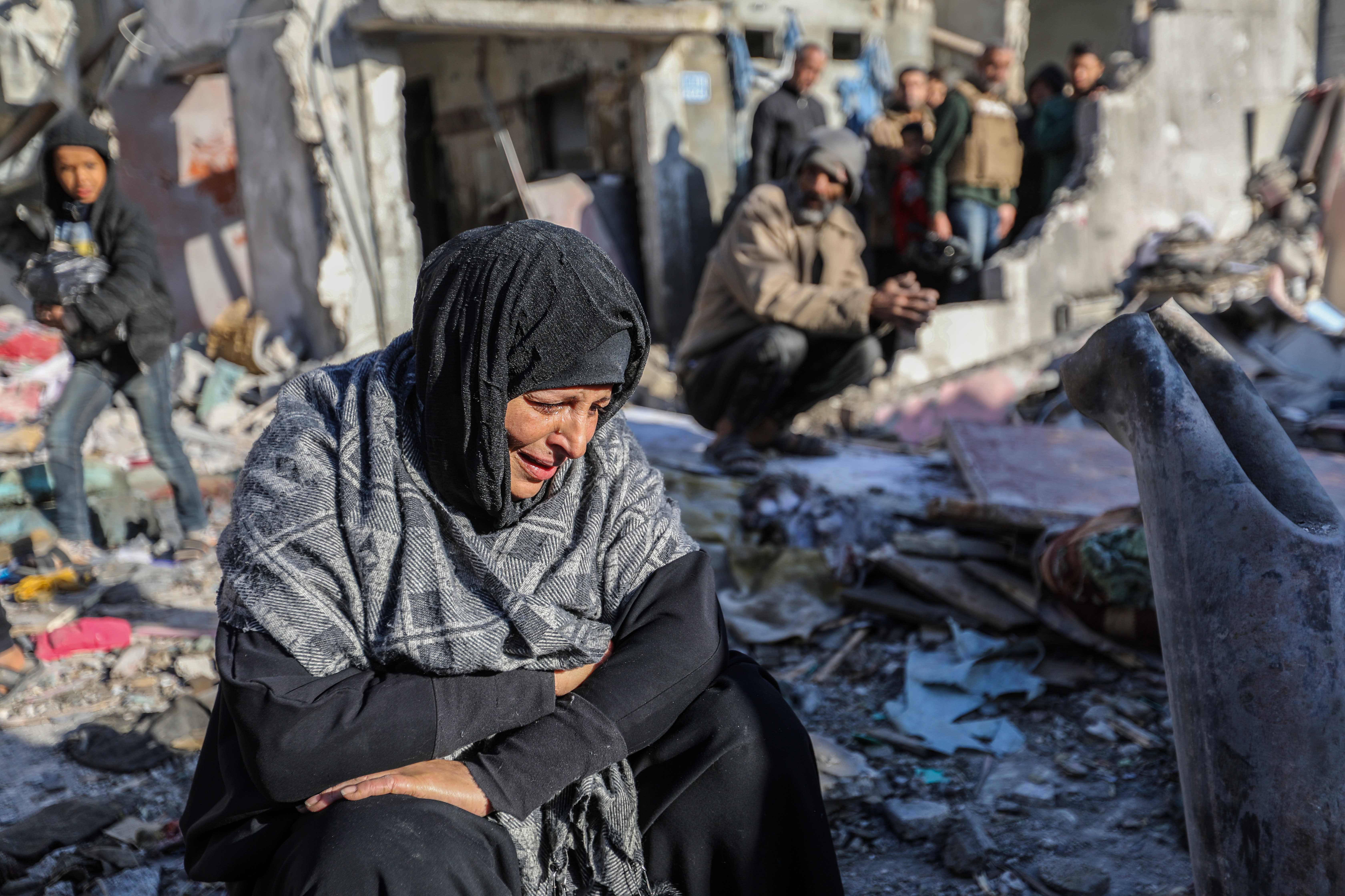 A woman looking distraught among the rubble of destroyed buildings.